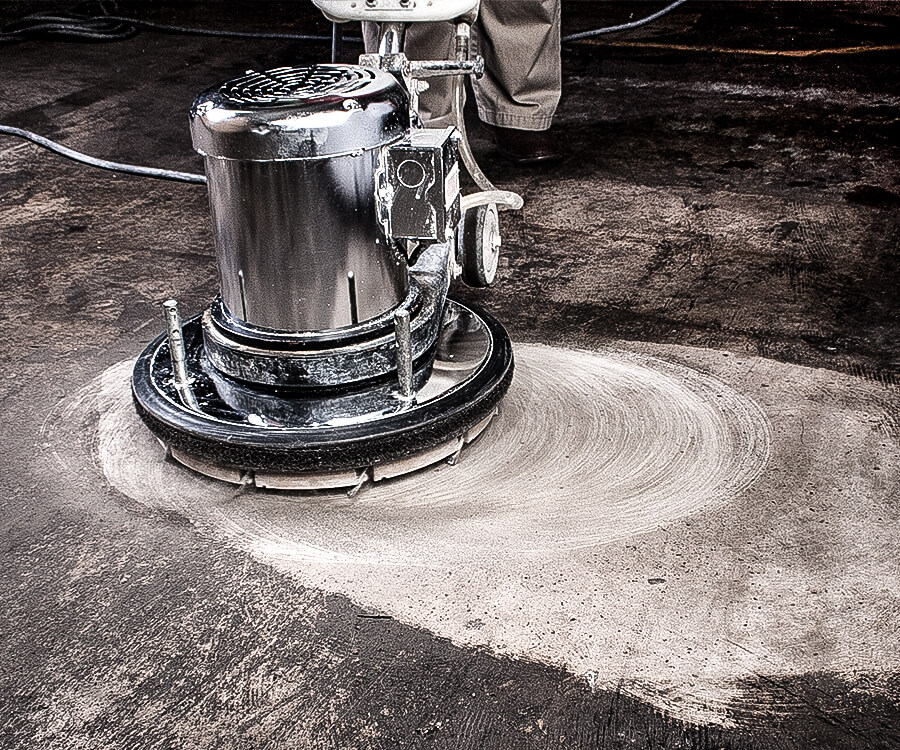 Industrial grinder removing old adhesive from concrete surface for flooring preparation.