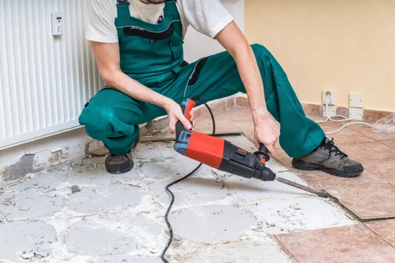 Worker using a power tool to remove tiles from a concrete floor, demonstrating tile removal service for flooring preparation.