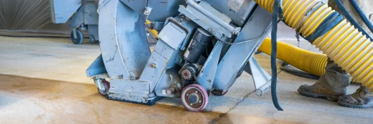 Concrete surface preparation equipment for shot blasting, showcasing machinery and dust extraction hose, emphasizing industrial flooring services.