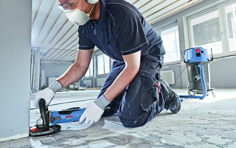 Worker using a Bosch concrete grinder for surface preparation, focusing on precise grinding and dust control in a renovation setting.